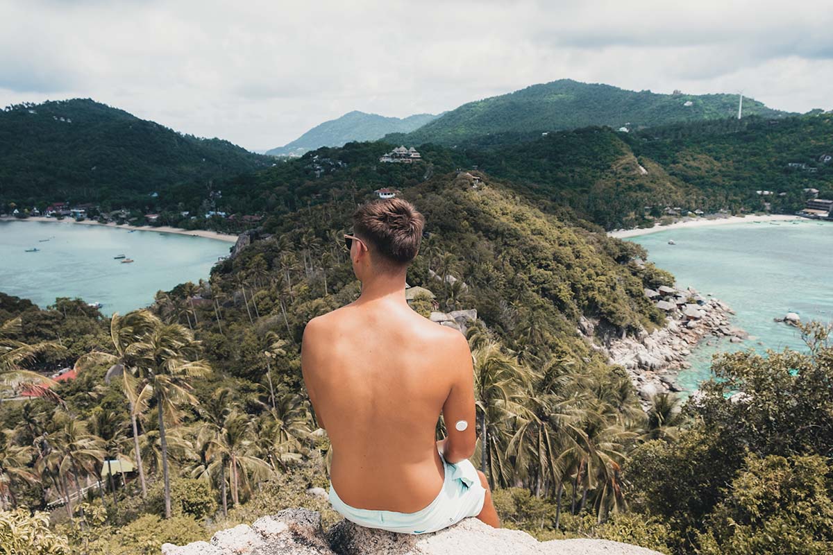 A tourist sitting at the John Suwan Viewpoint looking out at the distant Chalok Baan Kao Bay and Shark Bay which are split by a palm tree covered ridge