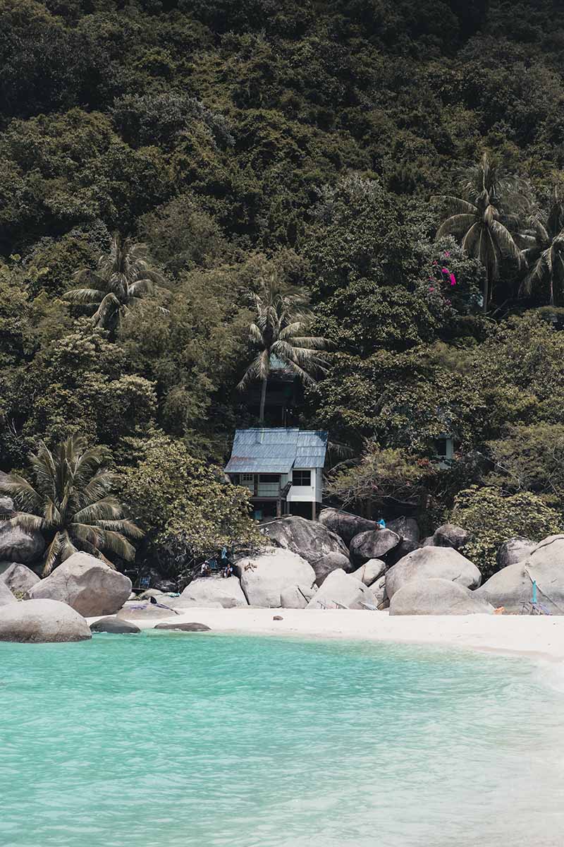 Koh Nang Yuan's turquoise water, and white sand beach outlined by boulders with a small hut perched on top surround by jungle