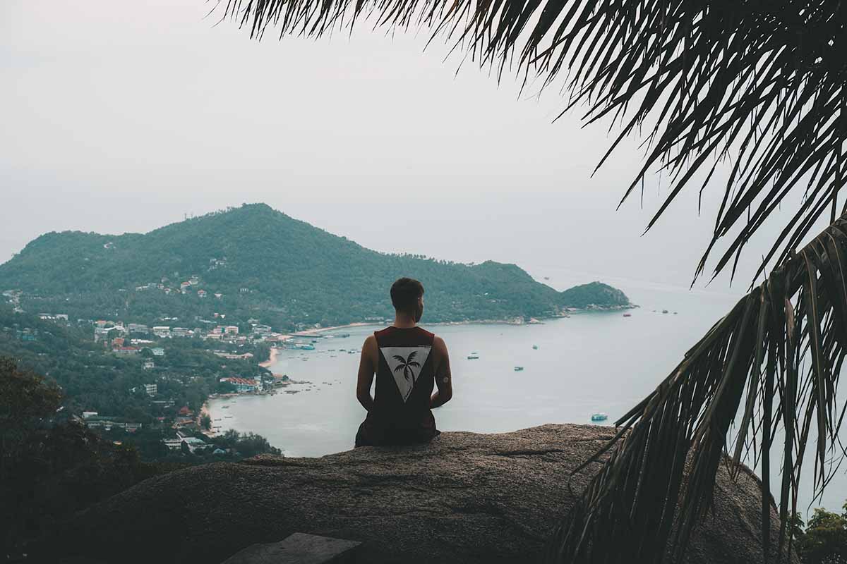 A tourist sitting at Summit Viewpoint looking out at the West coast beaches and jungle-covered south of Koh Tao