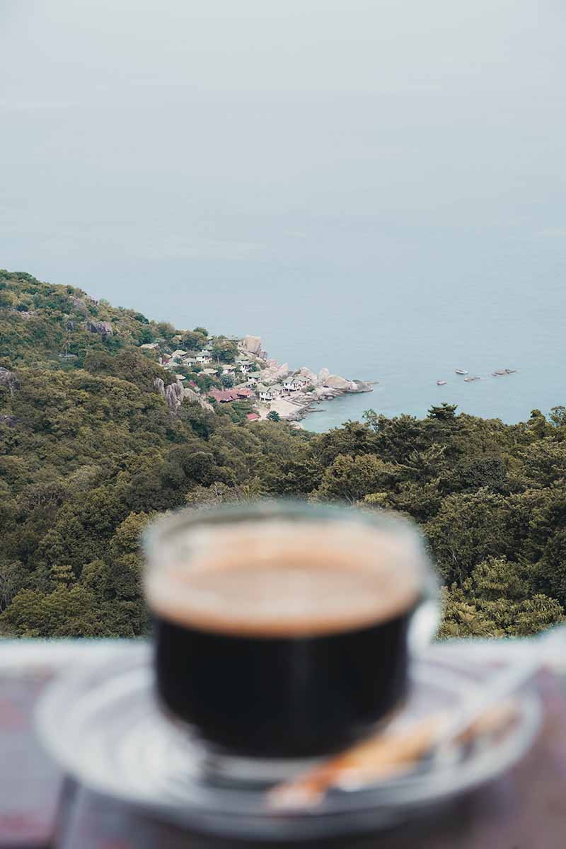 A cup of black coffee at the Love Koh Tao Viewpoint with the jungle-covered east coast of Koh Tao in the background