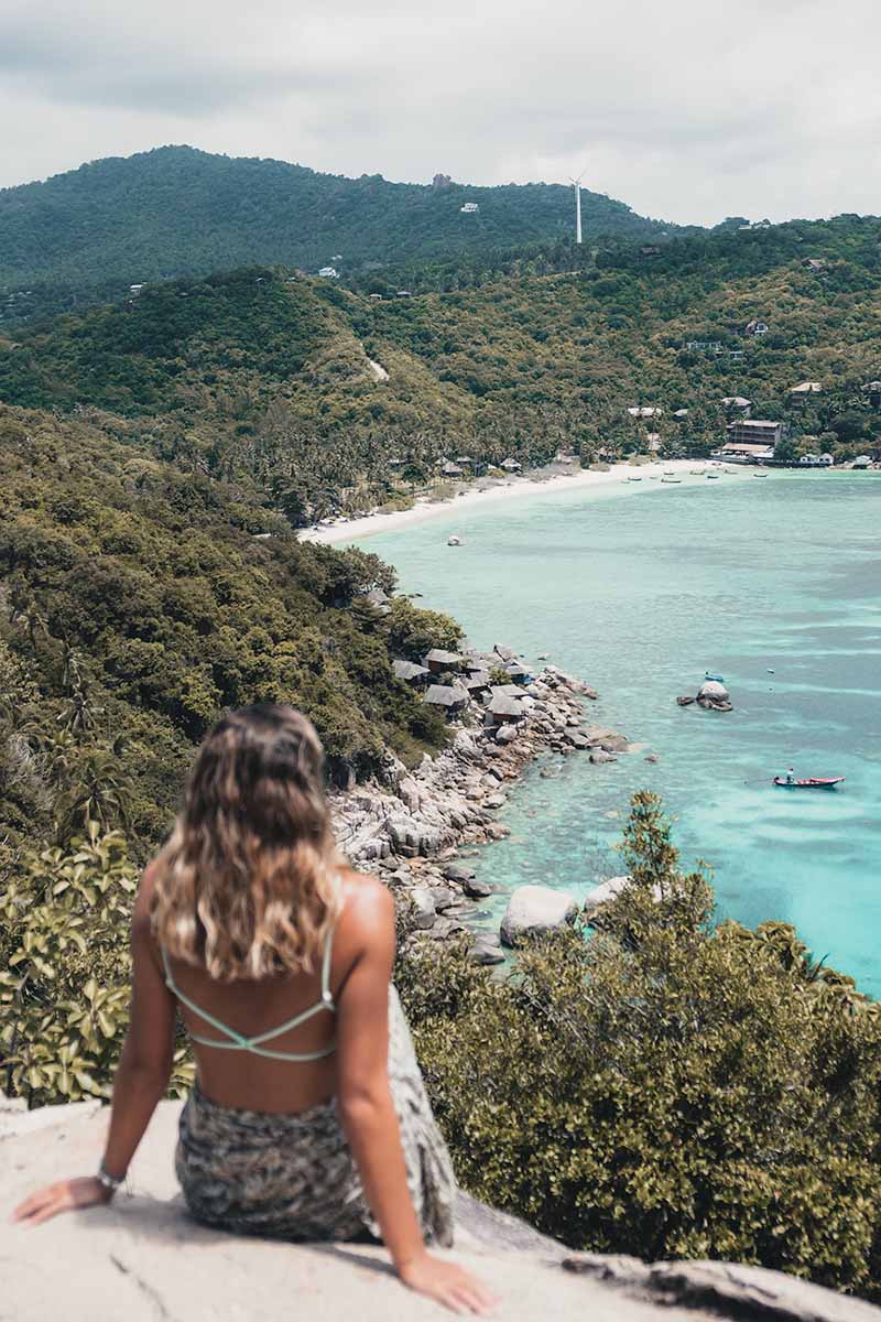 A tourist sitting at John Suwan Viewpoint looking out at the white  beach, turquoise water, rocks and jungle surrounds of Shark Bay