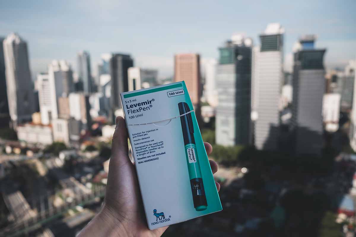 A box of green Levemir insulin FlexPens being held with the skyline of Kuala Lumpur in the background