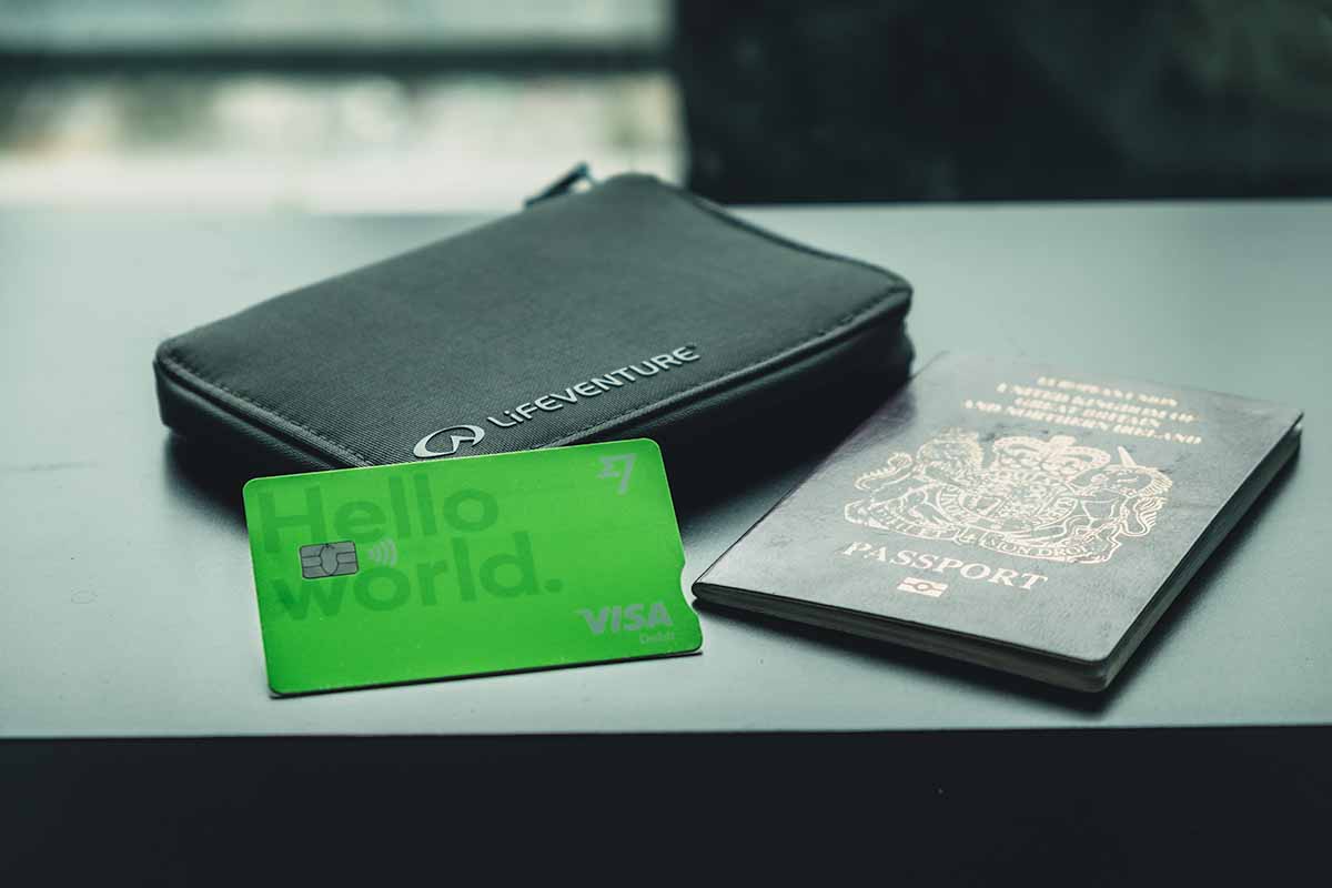 A green Wise debit card, a United Kingdom passport and a passport holder laid out on a dark coloured table with a blurred background