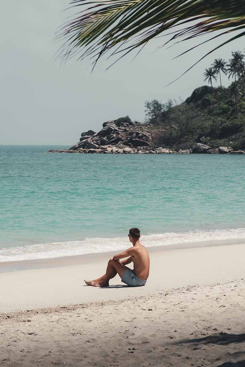 A tourist sitting on Bottle Beach's white sand.