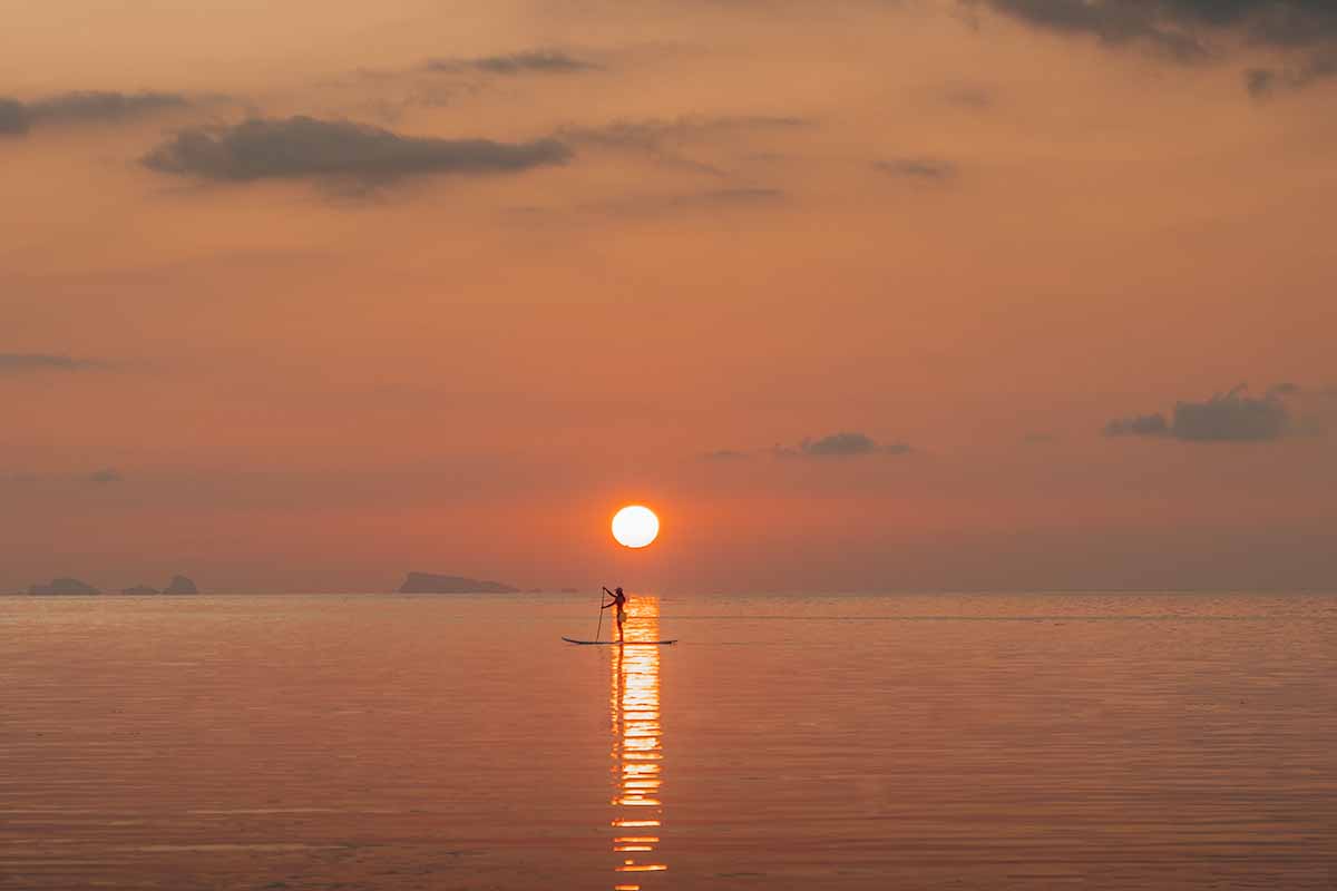 A paddle boarder gliding over the reflection of the sun on the water at Haad Yao.
