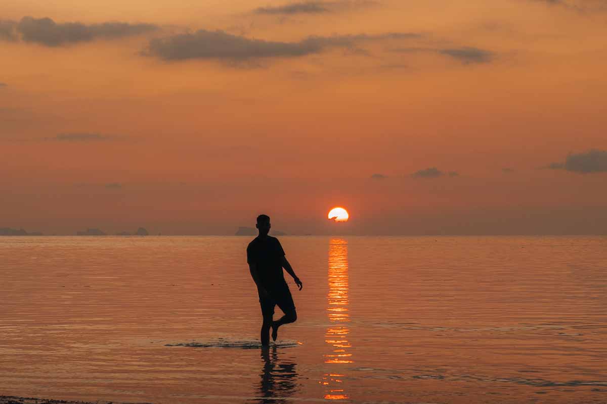 A tourist walking in the sea next to the reflection of the sun at Haad Yao.