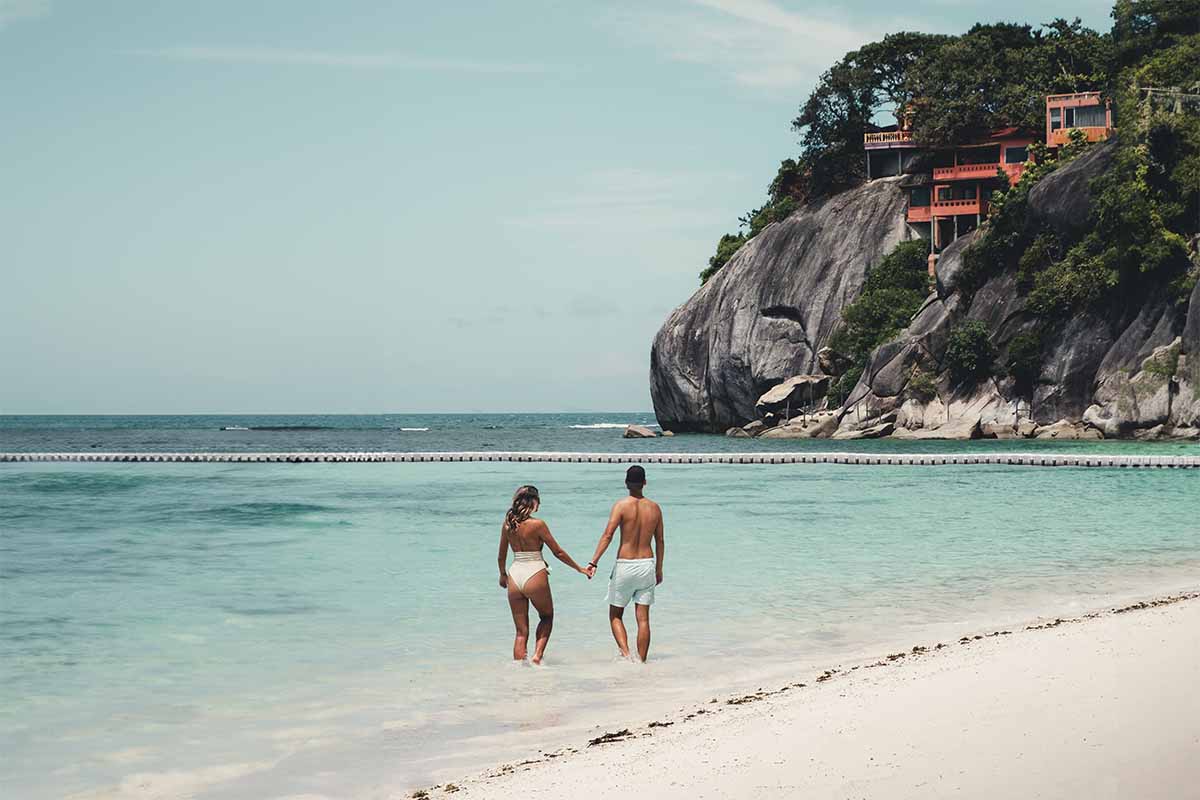 Two tourists holding hands while standing ankle-deep in the water at Leela Beach.