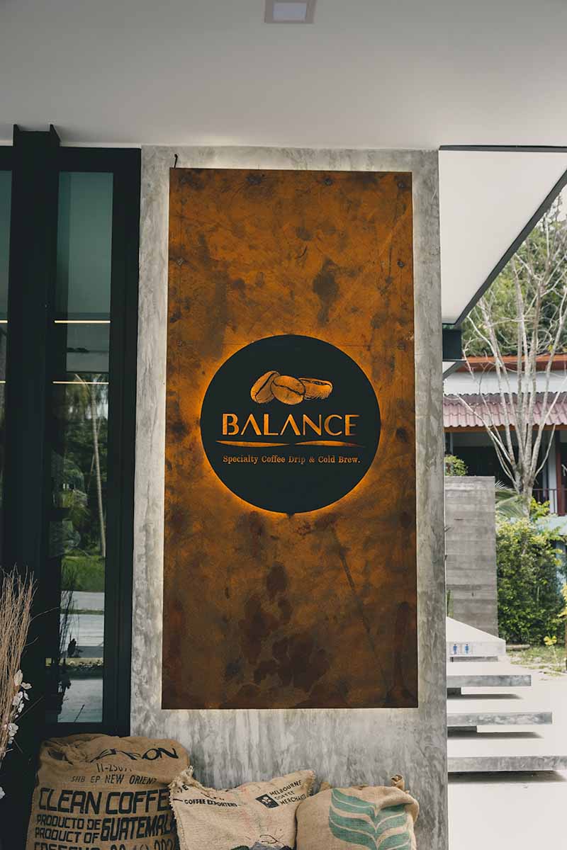 Black and orange sign with coffee bean logo that reads 'Balance Speciality Coffee Drip & Cold Brew' on a wall outside the cafe.
