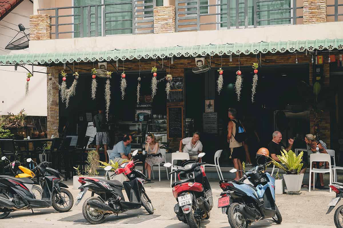 The front of the German Bakery by Achim with customers sitting and chatting at the outdoor tables and scooters parked along the roadside.