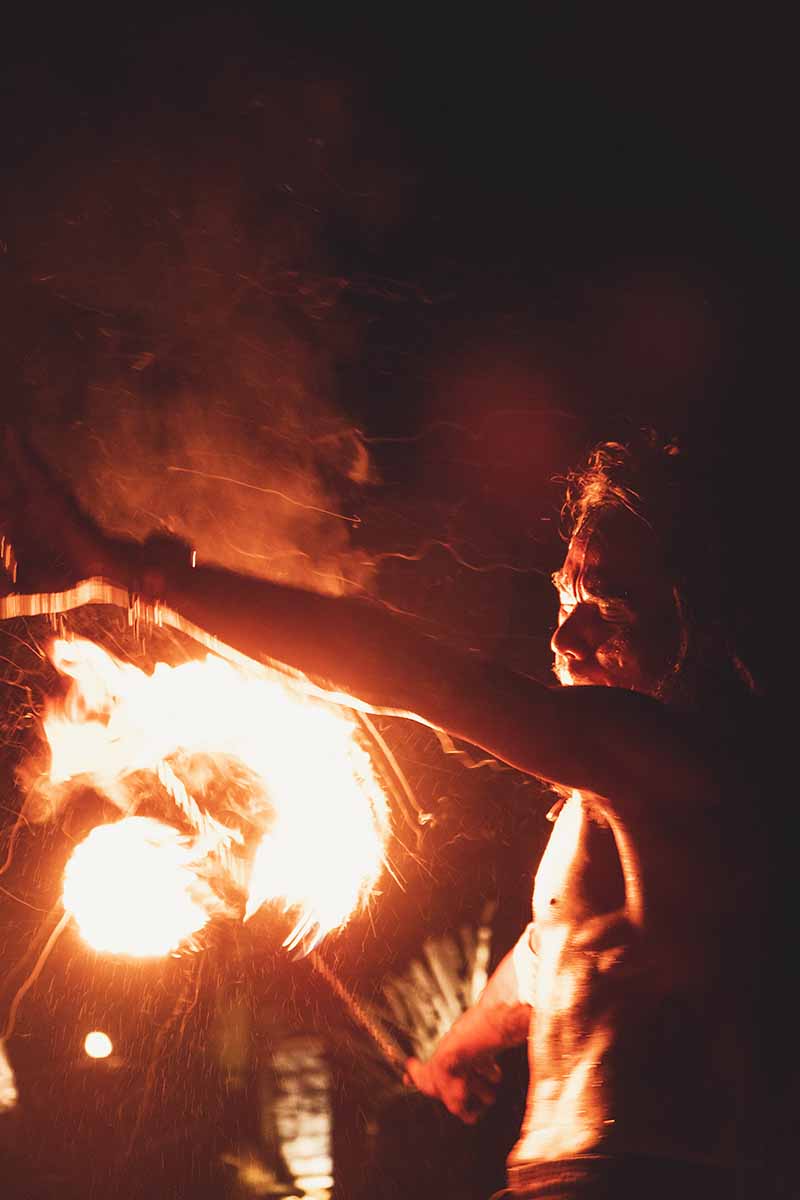 A fire performer spinning a fire ball close to his chest and face.