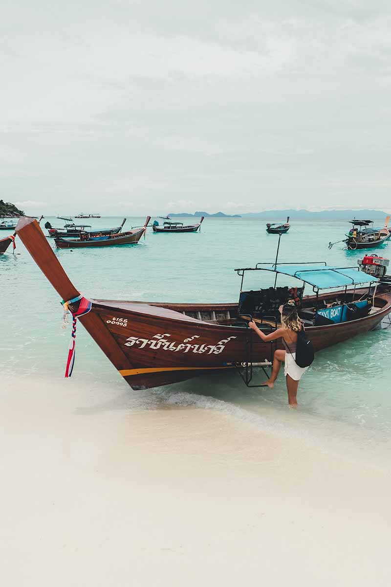 A female tourist climbing into a long-tail boat from the shallow water.