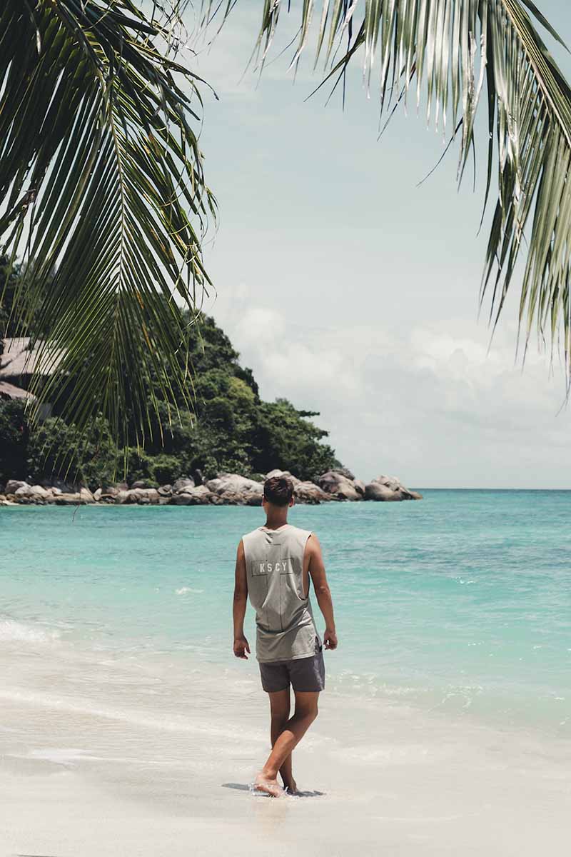 A male tourist walking towards the turquoise water of Sunset Beach.