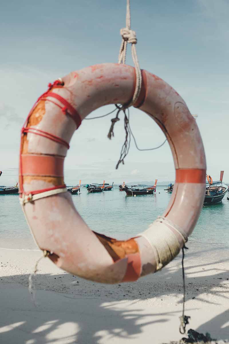 Long-tail boats anchored in the sea, framed through the centre of a hanging life saving buoy in the foreground.