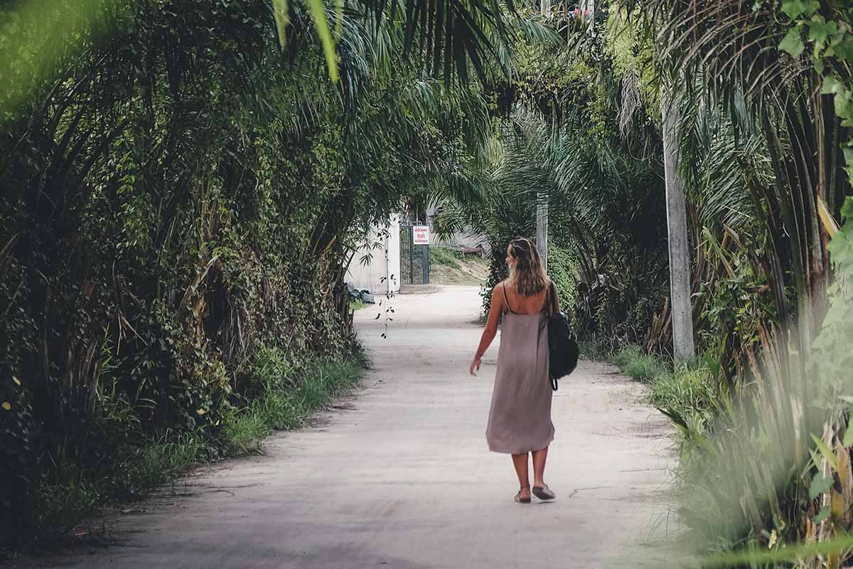 A female tourist walking along one of Koh Lipe's paved roads which is lined with green shrub.