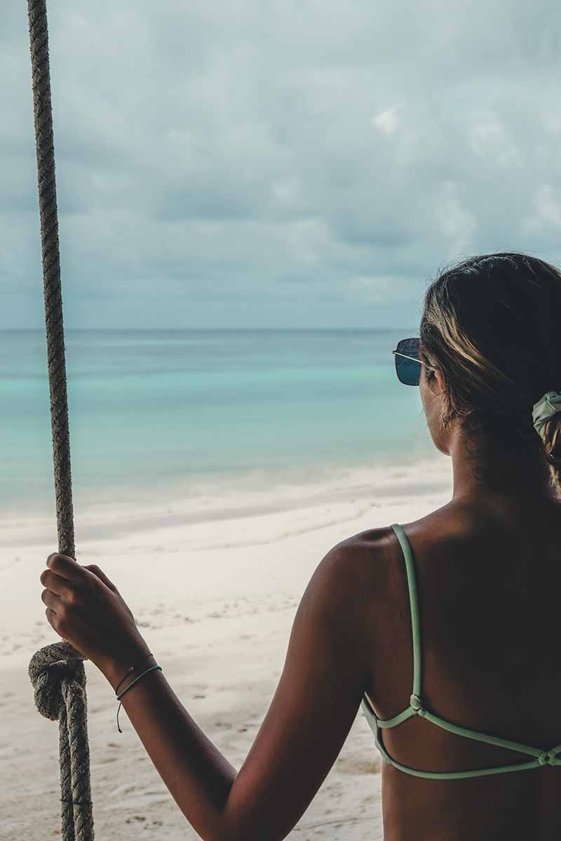 A female tourist sitting on a swing on the beach.