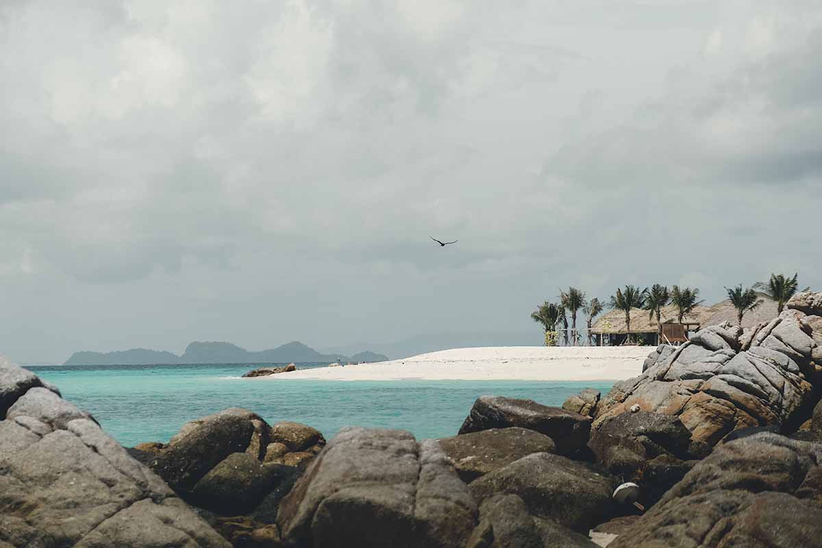 A bank of white sand at the northern tip of Sunrise Beach fringed with palms trees and wooden huts.