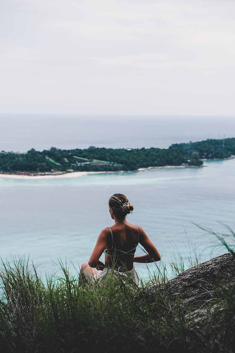 A female tourist sitting at the Koh Lipe viewpoint, with part of Koh Lipe in the distance.