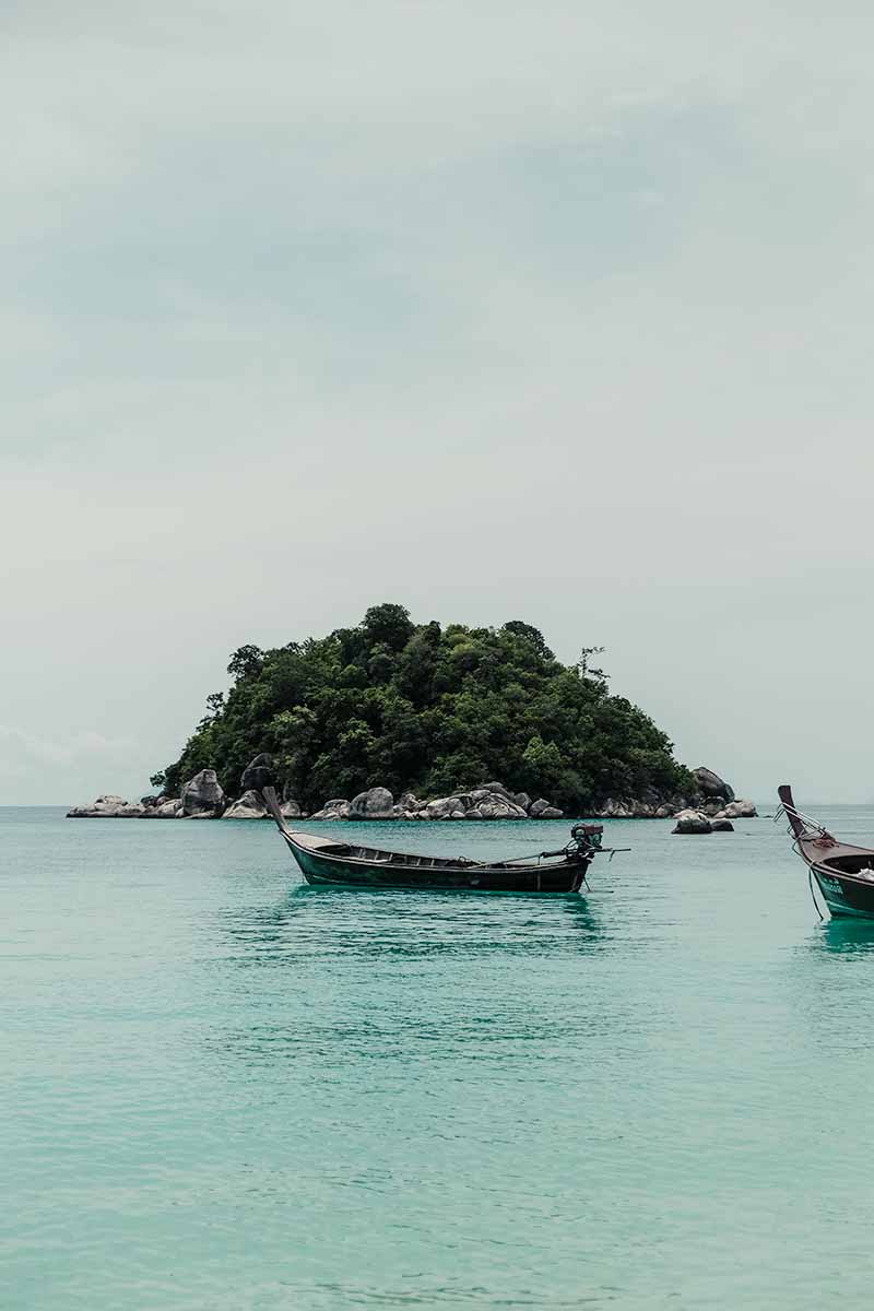 A long-tail boat anchored in the sea with the tiny island of Koh Usen in the background.