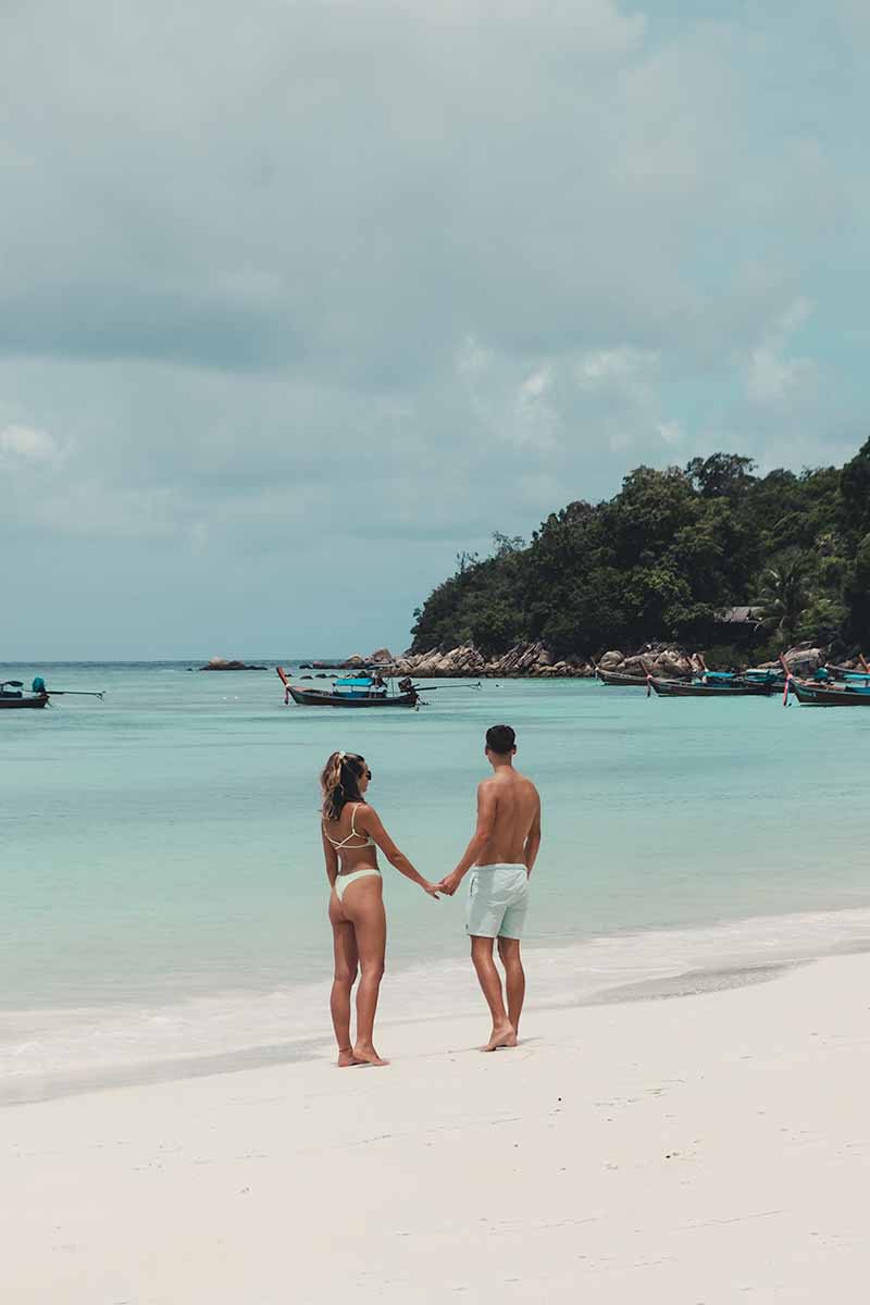 A couple holding hands while standing at the shoreline of Pattaya Beach.