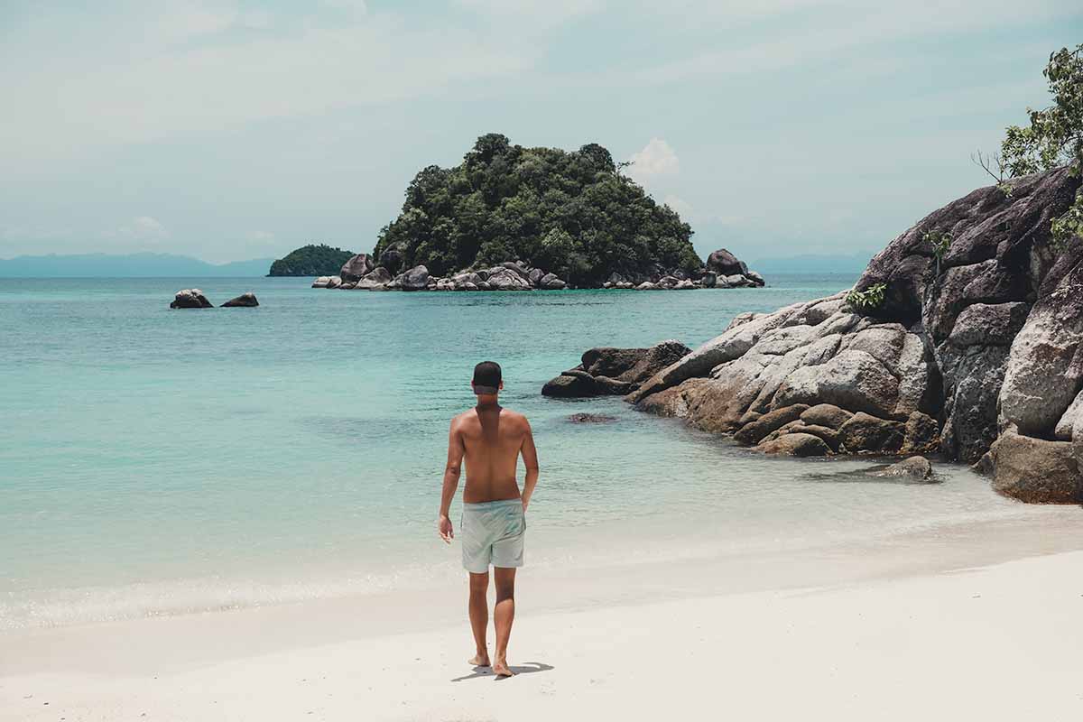 The back of a tourist walking towards the water on Sunrise Beach.