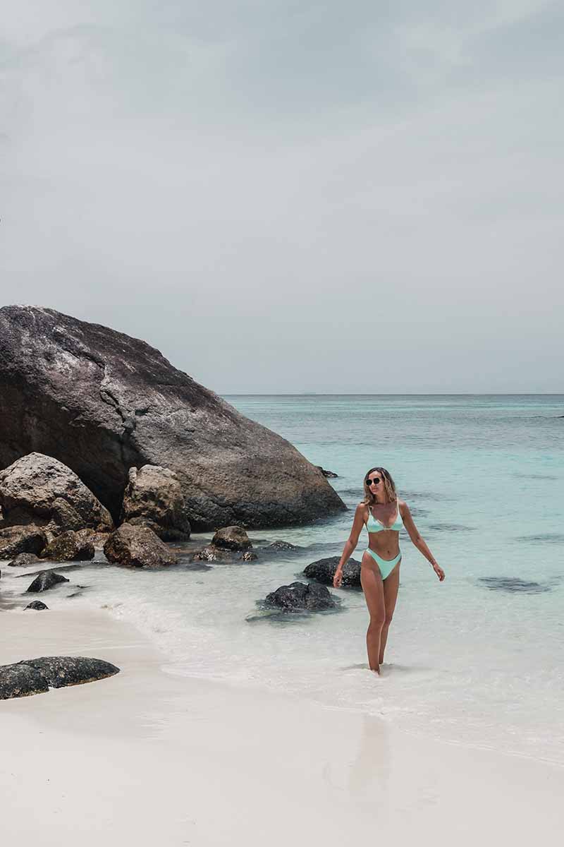 A female tourist standing ankle-deep in the sea in front of the picturesque boulders that mark the edge of the bay outside Ten Moons Lipe Resort.