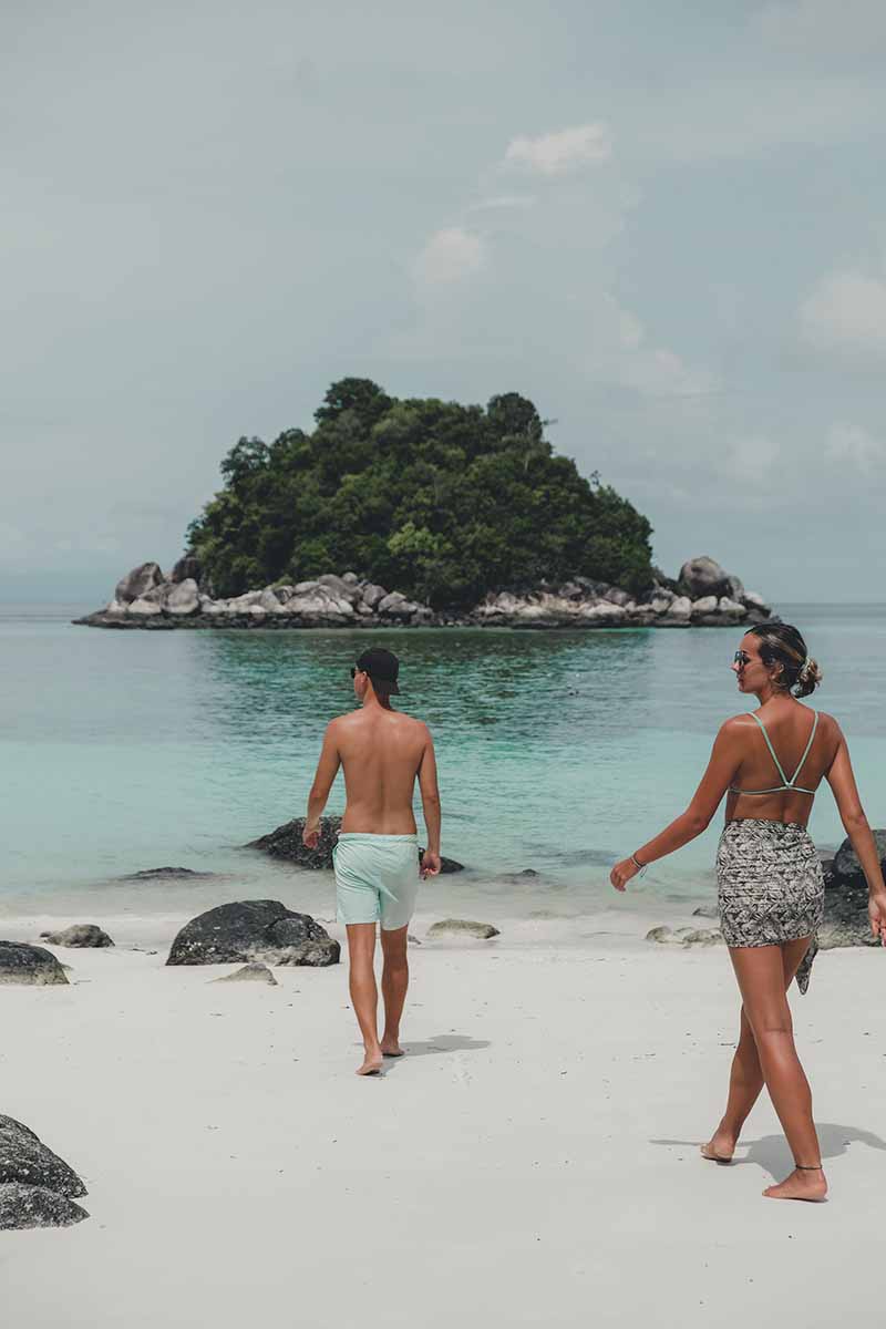 A couple walking towards the shoreline on Ten Moons Beach with the tiny island of Koh Usen in the distance.