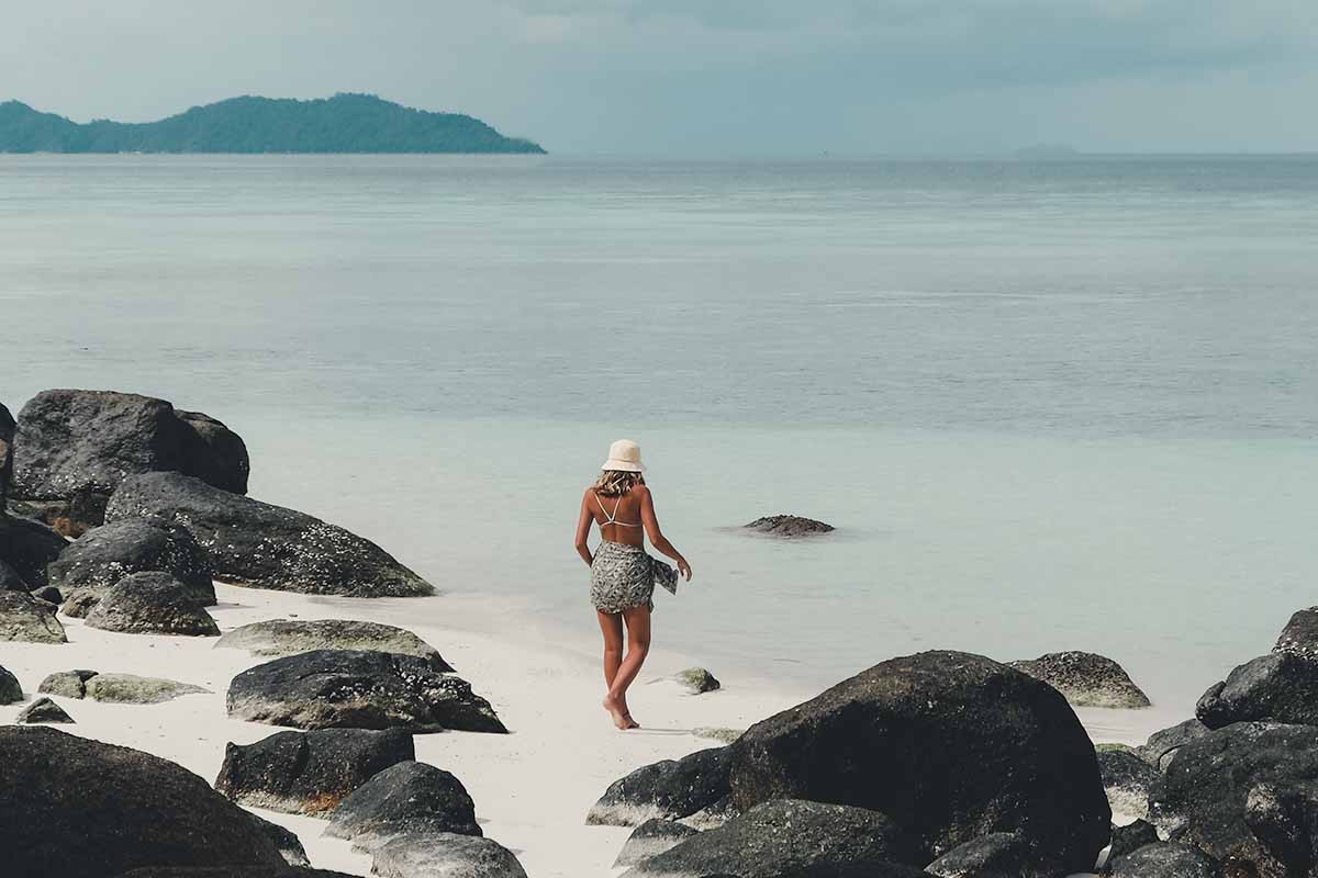 A female tourist walking towards the sea amongst rocks on the beach outside Ten Moons Lipe Resort.