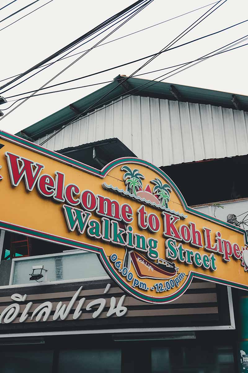 An orange, red and green sign at the entrance to Walking Street that says Welcome to Koh Lipe Walking Street 06.00pm - 12.00pm.