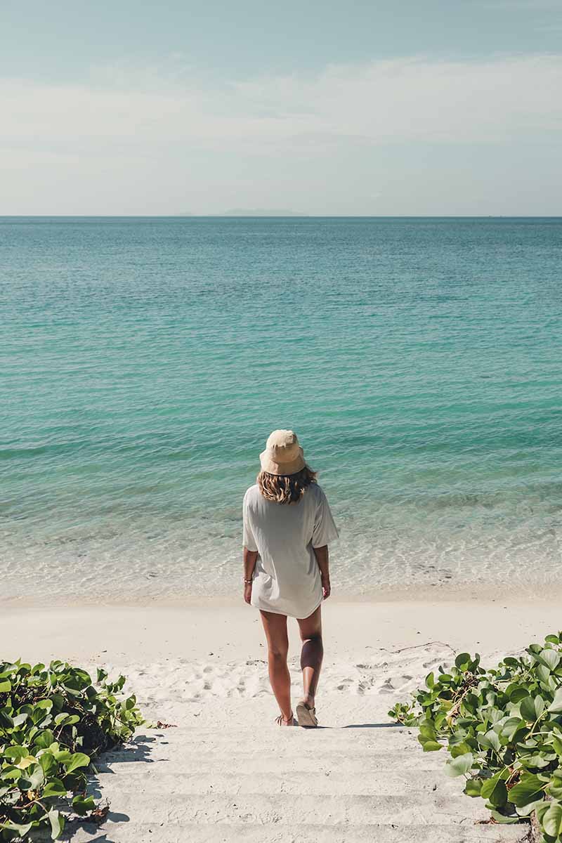 A woman walking down steps that lead down to the white sand and calm water of Chaloklum Beach.