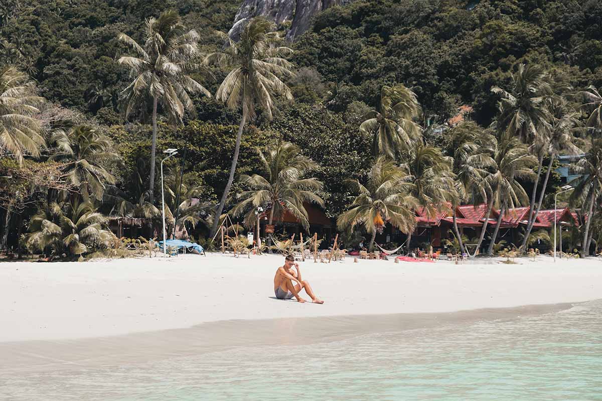 A person sitting on the white sand of Koh Phangan's palm tree-lined Haad Rin.