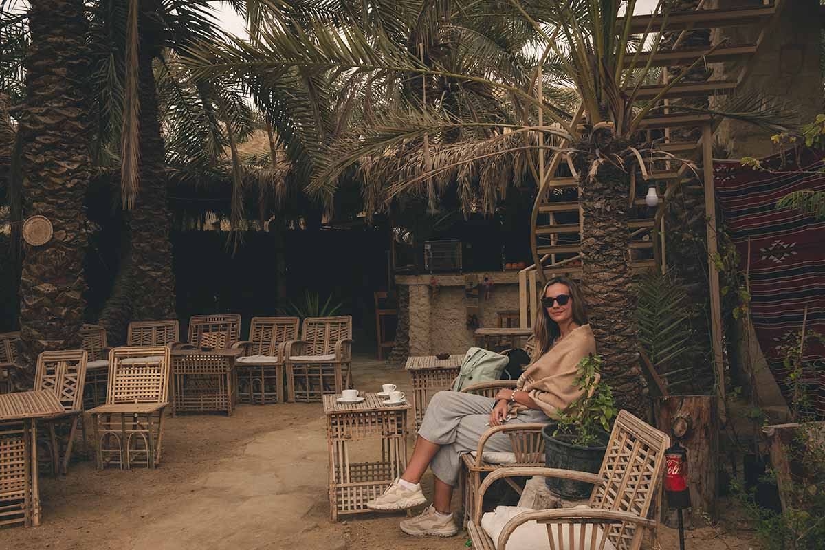 A woman sitting in an outdoor cafe at a table with three cups of coffee.