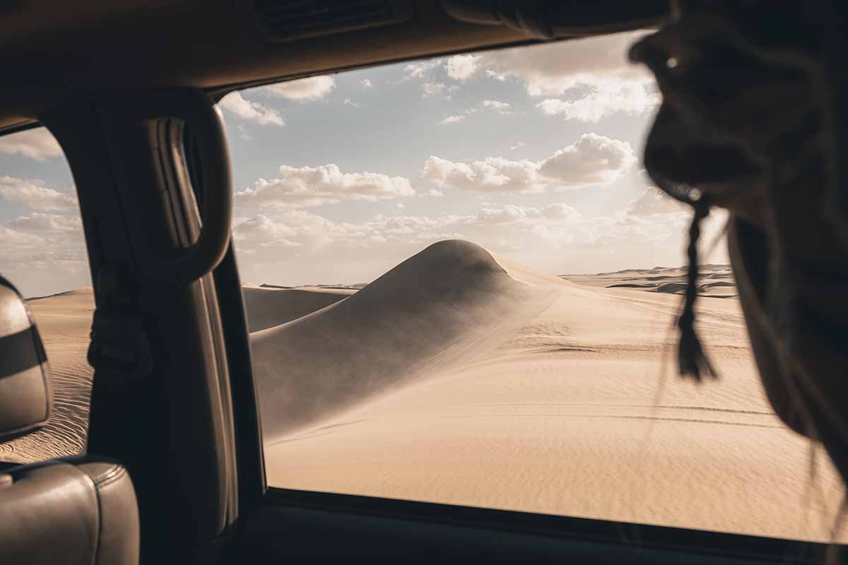 A person looking out at a large sand dune from the inside of a jeep in the Sahara Desert.