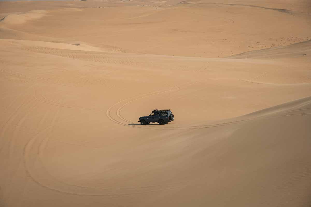 A jeep sitting at the bottom of a sand dune surround by the vast sand of the Great Sand Sea.