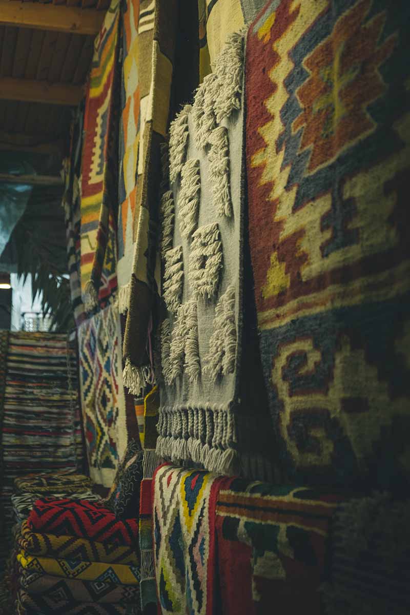 Several patterned and colourful rugs hanging on the wall inside a souvenir shop.