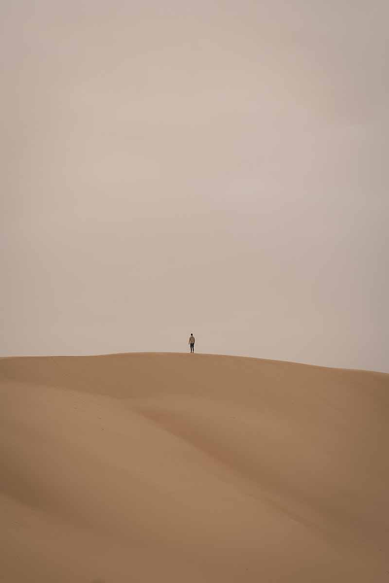 A person standing at the top of a large sand dune.