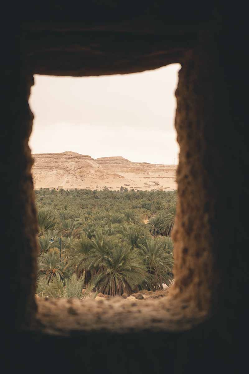 A view of Dakrur Mountain and sea of palm trees seen through an open stone window.