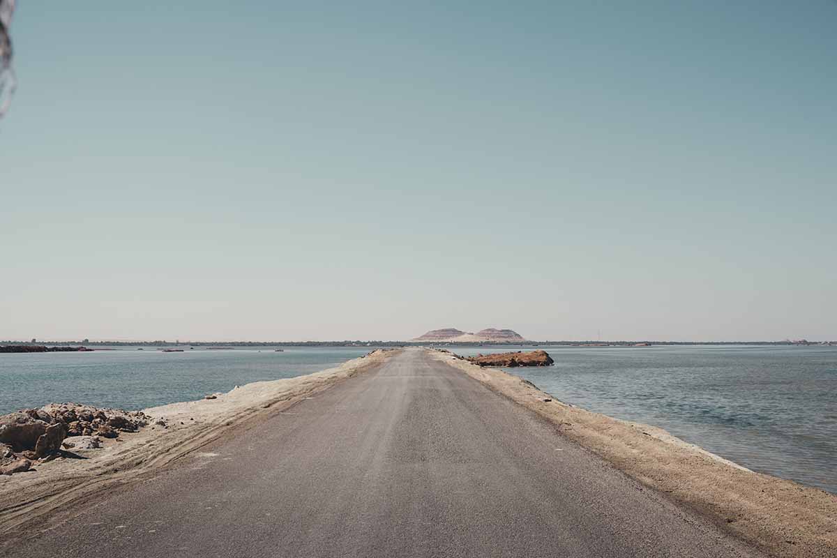 A narrow strip of road leading into the distance with large bodies of water on either side.