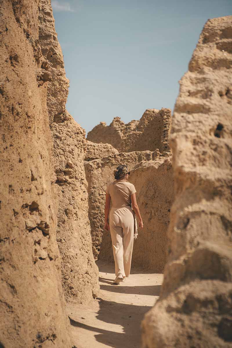 A woman walking through a narrow alley within the mud-brick ruins of Shali Fortress.