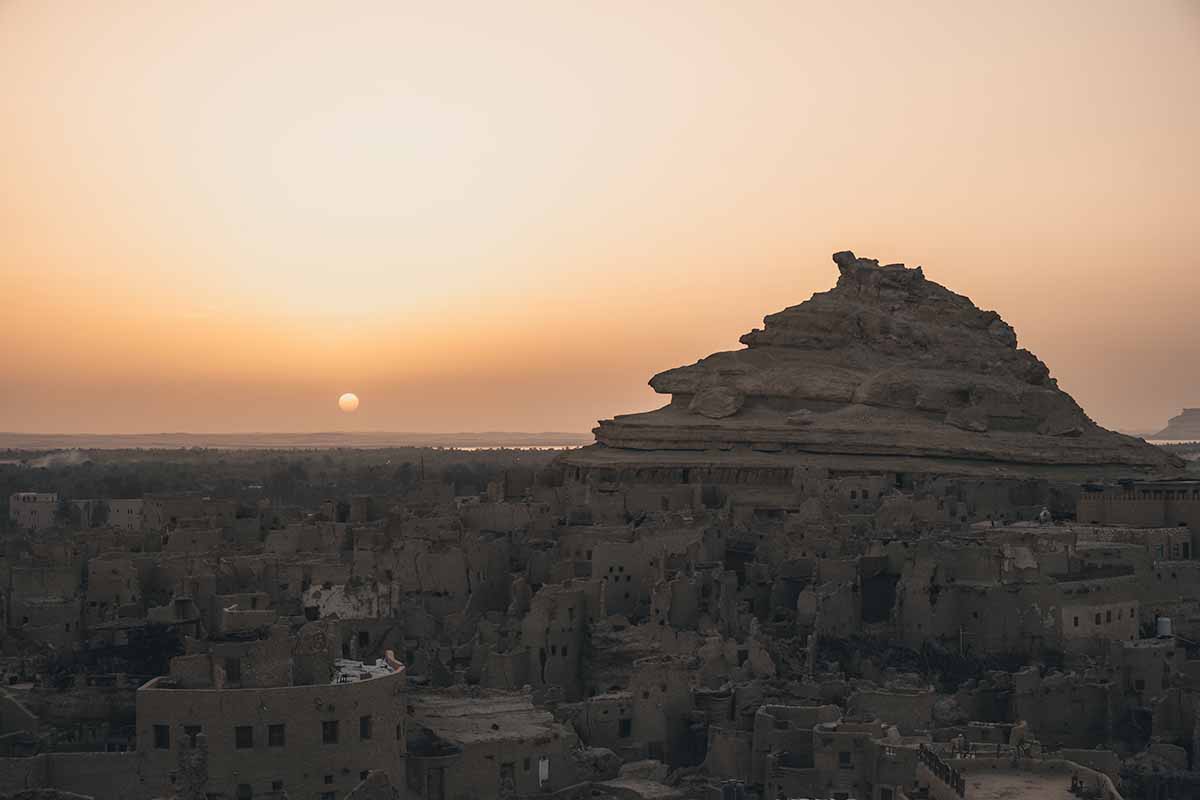 The sun about to drop below the distant dunes of the Sahara Desert seen from Shali Fortress.