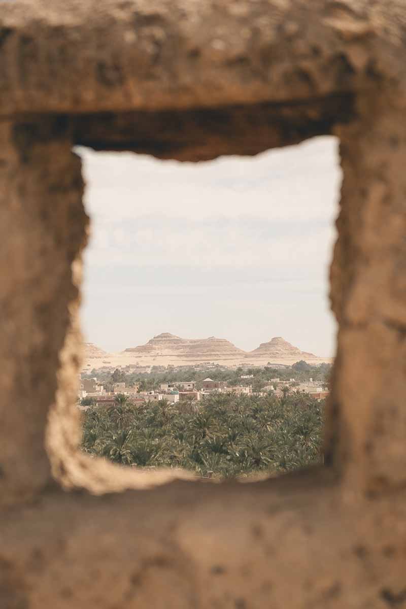 An open stone window of Shali Fortress looking over the distant Dakrur Mountain, sea of palm trees and village.