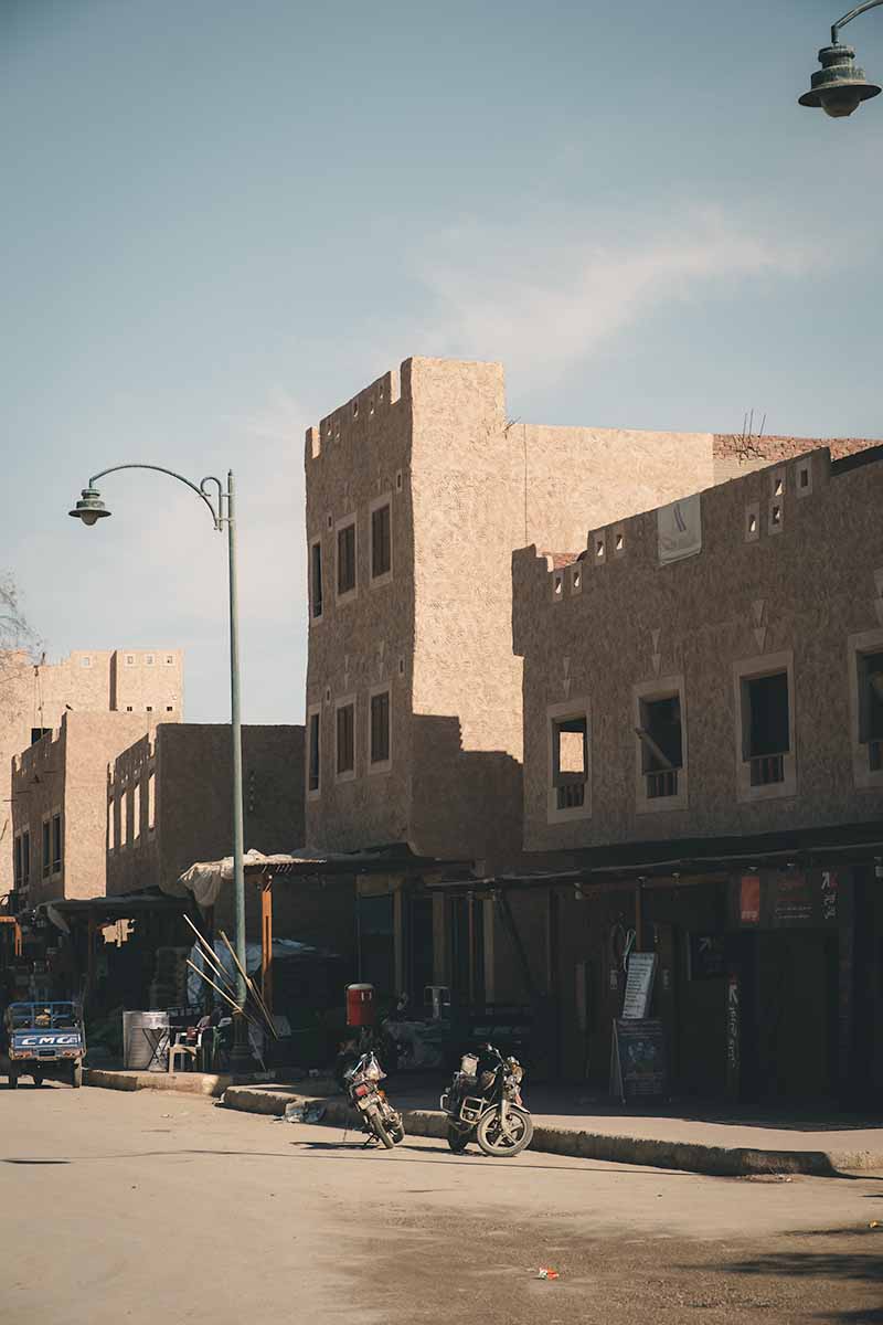 A dusty street, with two parked motorbikes and mud-brick buildings in Siwa's town centre.