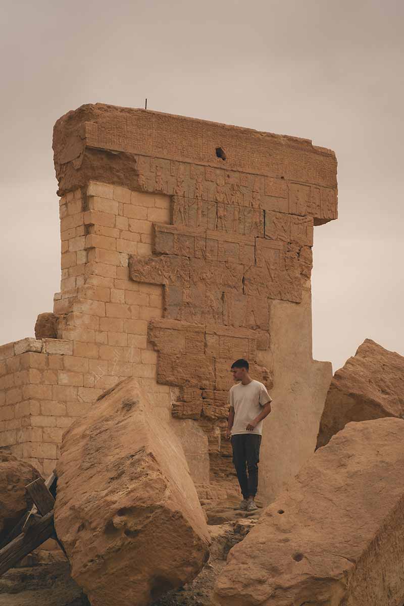 A man standing in front of the last wall that remains standing at the Temple of Umm Ubayd.