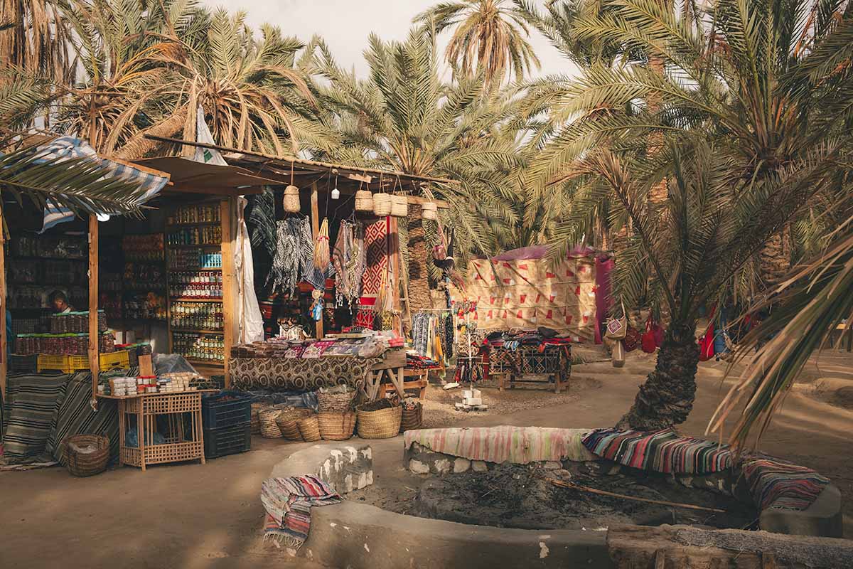 A rustic local souvenir shop backed by palm trees selling scarfs, rugs, spices and more.