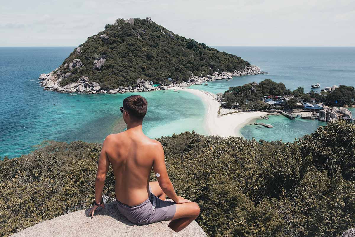 A man sitting at the Koh Nang Yuan viewpoint, looking over the narrow strip of white sand connecting two other islets.