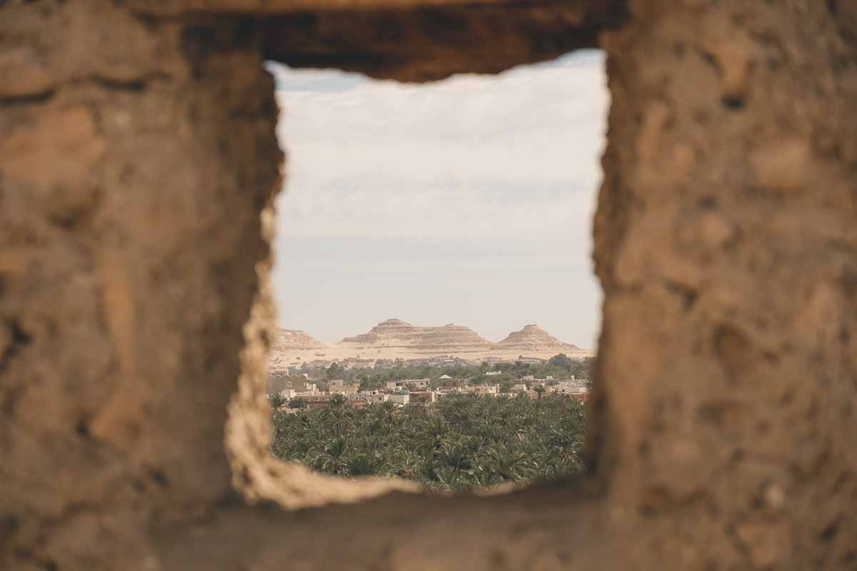 Dakrur Mountain and a sea of palm trees seen through a rocky frame where a window used to be.