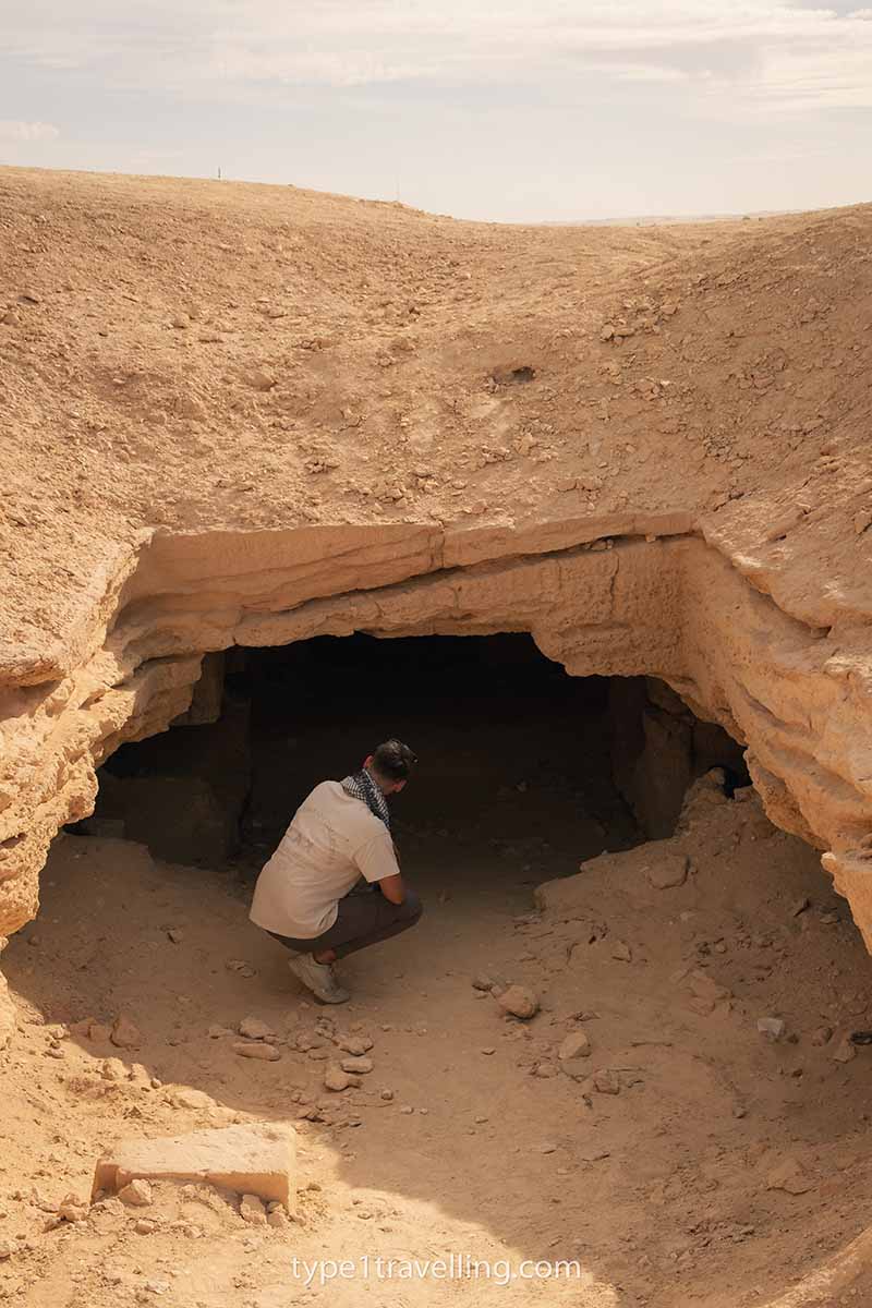 A man crouched and looking into a dark cavern.