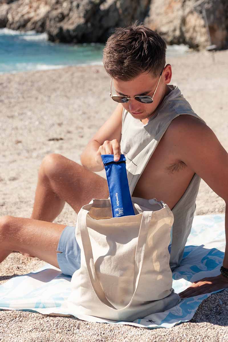 A man pulling a 4ALLFAMILY Chiller travel case out of a tote bag while sitting on the beach.