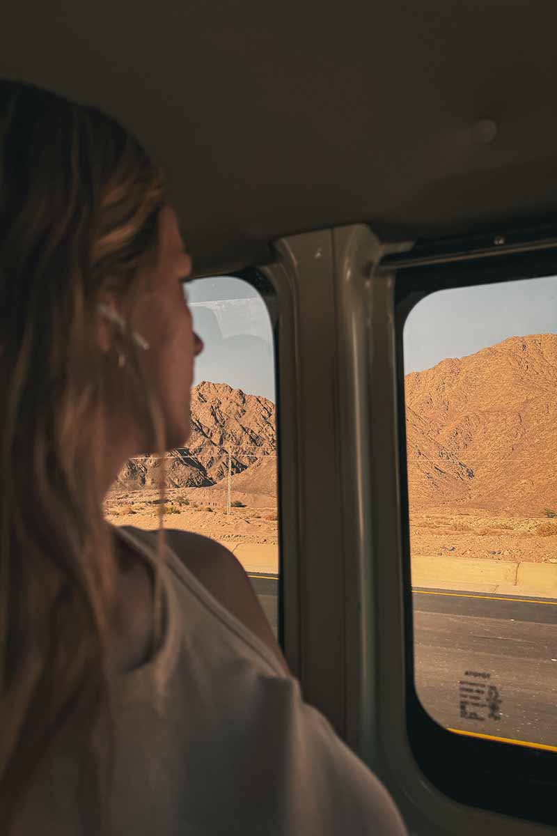 A woman looking out of a minivan window at the rocky mountain landscape.