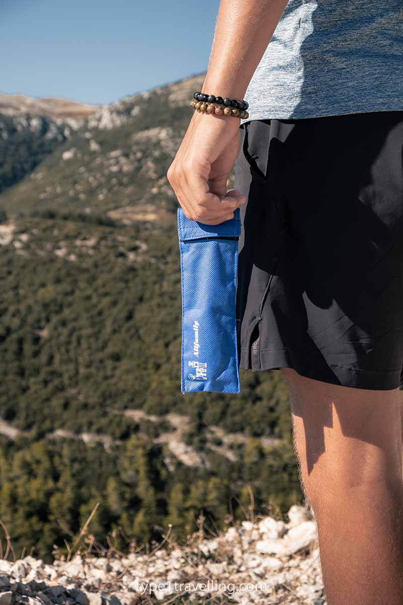 A person holding a 4ALLFAMILY Chiller travel case by their side in a mountain landscape.