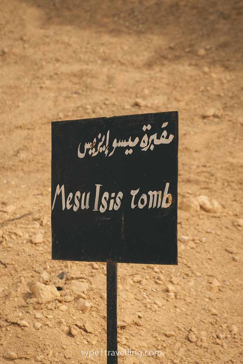 A black sign which reads Mesu Isis Tomb in English and Arabic.